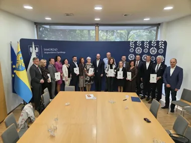 Grupa osób pozuje do pamiątkowego zdjęcia z dyplomami przed banerem Samorządu Województwa Opolskiego w sali konferencyjnej.